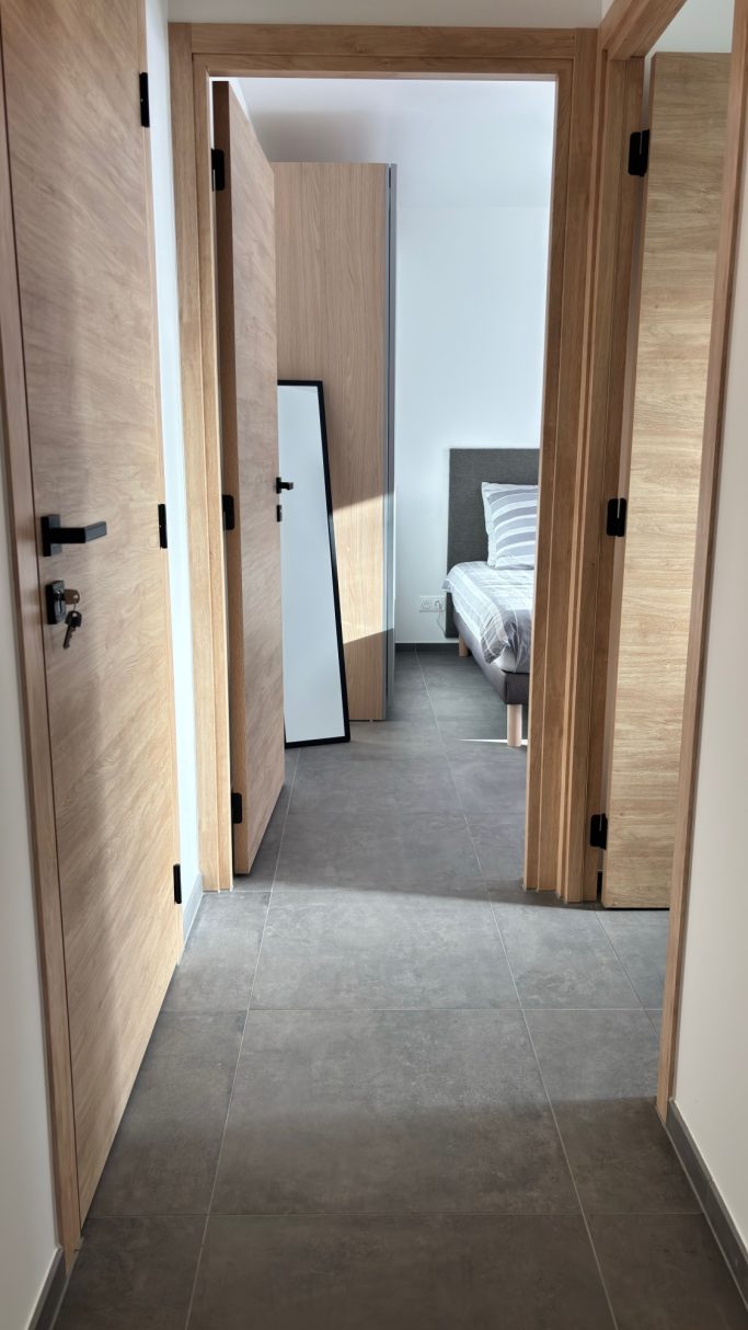 Couloir lumineux avec deux portes ouvertes menant à une chambre et un miroir.
